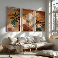 three paintings hang on the wall above a white couch in a room with large windows