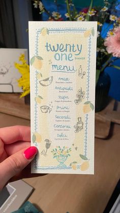 a person holding up a card with the words twenty one menu on it in front of flowers