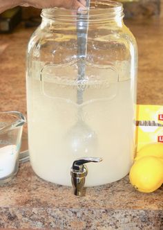 a person is filling a glass jar with water and lemons on the counter top