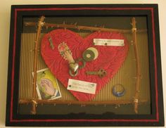 a red heart in a shadow frame with keys and other items attached to the sides