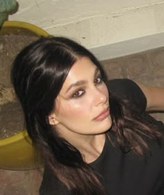 a woman with long dark hair sitting on the ground next to a potted plant