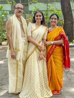 three people standing next to each other in yellow and orange sari outfits, posing for the camera