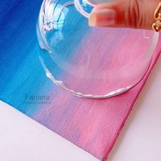 a hand is touching the bottom of a wine glass on top of a pink and blue napkin