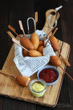 some food is sitting on a cutting board with dips and sauces in bowls