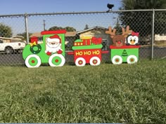 two wooden christmas train decorations sitting on top of a grass covered field next to a chain link fence