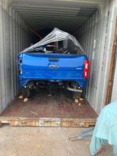 the back end of a blue pickup truck in a shipping container with it's hood up