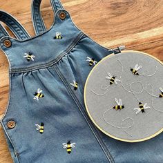 a pair of denim overalls with embroidered bees on them next to a handmade embroidery bee pin cushion