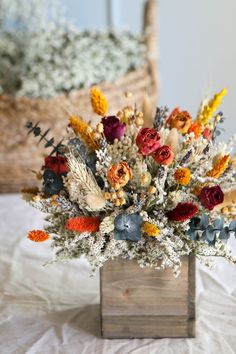 an arrangement of flowers in a wooden vase on a white tableclothed bed sheet