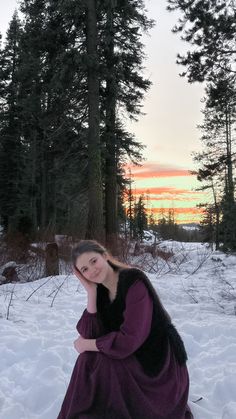 a woman sitting in the snow wearing a purple dress