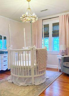 a white crib in the middle of a room with pink curtains and furniture around it