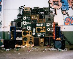 many speakers stacked on top of each other in front of a wall with grafitti