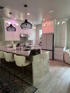 a kitchen with marble counter tops and white chairs in front of an island that's surrounded by pink cabinets