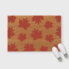 a pair of white shoes sitting on top of a brown rug with red maple leaves