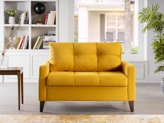 a yellow couch sitting in front of a white book shelf next to a potted plant