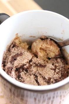 a cup filled with brownie crumbs on top of a wooden table next to a spoon