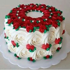 a white cake with red and green frosting roses on the top is sitting on a plate