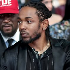 a man with dreadlocks sitting in front of another man wearing a red hat