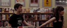 a man and woman standing in front of a bookshelf full of books, holding hands