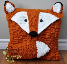 a crocheted fox pillow sitting on top of a wooden floor