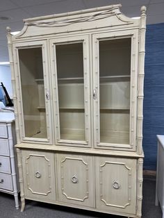 a white china cabinet with glass doors and drawers in an office setting, next to a blue wall