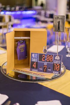 the table is set up for an event with purple and yellow jerseys on display in a cardboard box