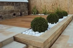 a wooden planter filled with plants next to a stone wall and wood decking