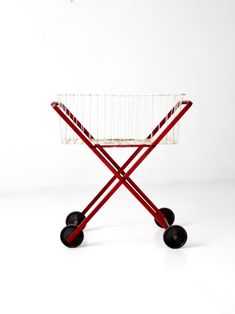 a red and white cart with wheels on a white surface in front of a wall