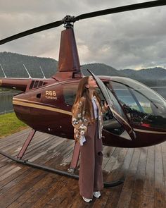 a woman standing in front of a helicopter on top of a wooden deck next to a lake