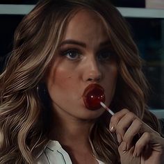 a woman with long hair is holding a red lollipop in her mouth