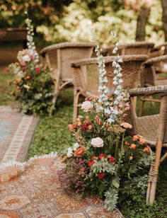 an outdoor ceremony with chairs, flowers and rugs on the ground in front of them