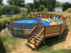 an above ground pool surrounded by wooden decking and blue lounge chairs on the lawn