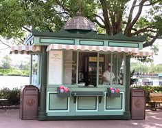 a small green and brown kiosk sitting on the side of a road next to a tree