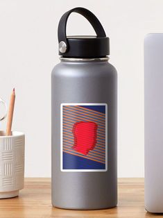 a red piece of artwork on a gray water bottle next to a white cup with a pencil in it