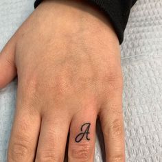 a person's hand with a small tattoo on their left thumb and the letter a tattooed across the middle finger