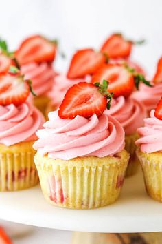 several cupcakes with pink frosting and strawberries on top are arranged in rows