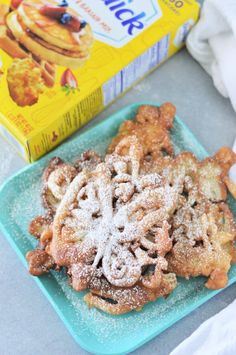 a blue plate topped with powdered pastry next to a carton of milk