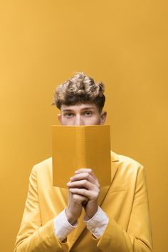 a young man in a yellow suit holding up a piece of paper to his face