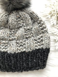 a gray and black knitted hat with a pom - pom on top