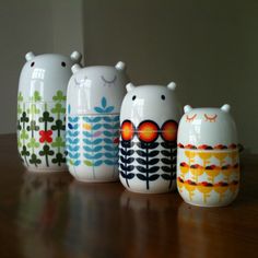 five ceramic owl figurines are lined up on a wooden table top, with one sitting in the middle