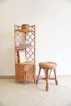 a wicker book shelf next to a small stool with a basket on top and a magazine rack in the corner