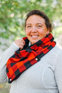 a smiling woman wearing a red and black plaid scarf around her neck with trees in the background