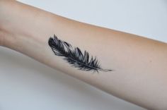 a woman's arm with a black feather tattoo on it