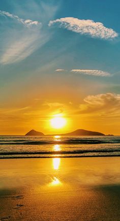 the sun is setting over an ocean with mountains in the distance and water reflecting on the sand