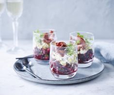 three glasses filled with food sitting on top of a metal tray next to two wine glasses