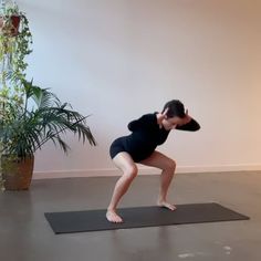 a woman standing on a yoga mat in front of a potted plant and stretching