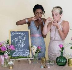 two women standing next to each other in front of a sign and table with flowers