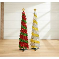 two small christmas trees are on display in front of a white wall and wooden floor