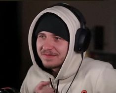 a man wearing headphones and a hoodie looks at the camera while sitting down