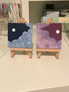 two small easels with paintings on them sitting on a table next to each other