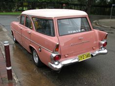 an old pink car is parked on the side of the road